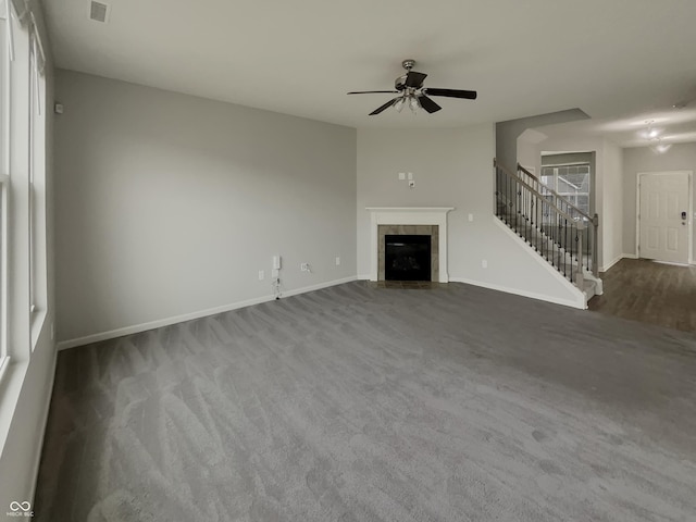 unfurnished living room with ceiling fan, a fireplace, visible vents, baseboards, and stairway