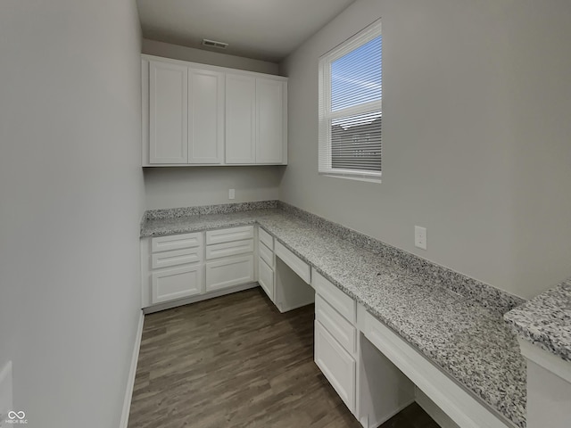 unfurnished office with dark wood-style flooring, built in study area, visible vents, and baseboards