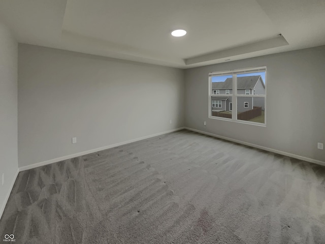 empty room featuring carpet floors, a tray ceiling, and baseboards