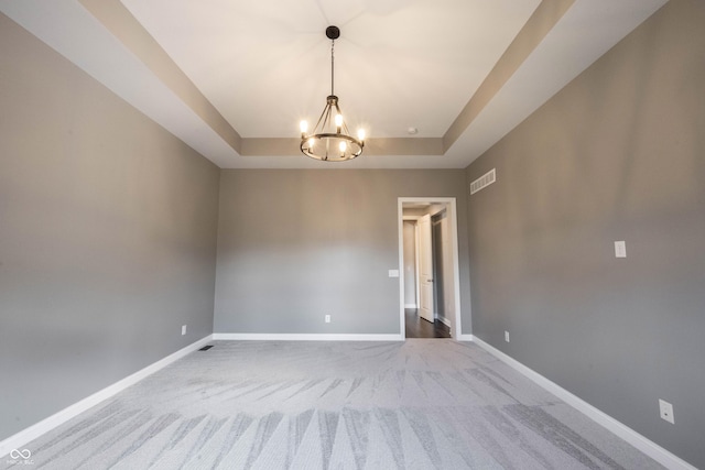 empty room featuring a raised ceiling, carpet flooring, a notable chandelier, and baseboards