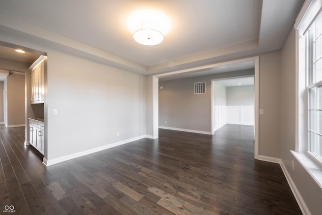 unfurnished room with a healthy amount of sunlight, baseboards, visible vents, and dark wood-style flooring