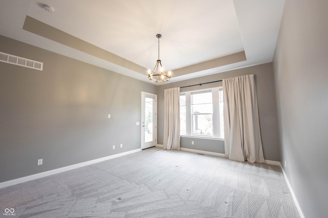 spare room with visible vents, a tray ceiling, baseboards, and light colored carpet