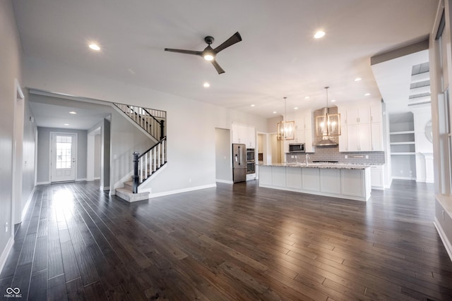 unfurnished living room with dark wood-style floors, recessed lighting, ceiling fan with notable chandelier, and stairs