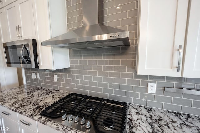 kitchen featuring stainless steel appliances, tasteful backsplash, white cabinetry, light stone countertops, and wall chimney exhaust hood