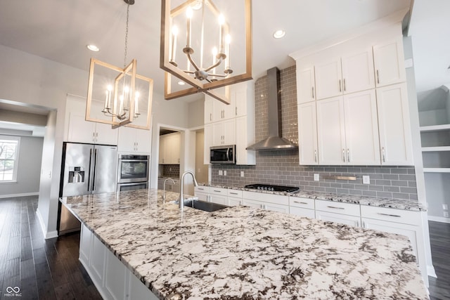 kitchen with appliances with stainless steel finishes, a sink, an inviting chandelier, wall chimney range hood, and backsplash