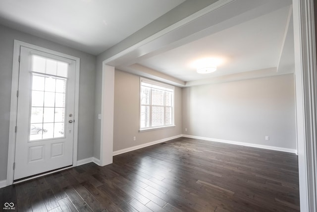 foyer entrance with a raised ceiling, dark wood finished floors, and baseboards