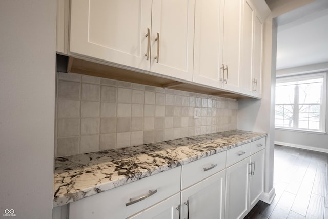 kitchen featuring light stone countertops, tasteful backsplash, white cabinetry, and baseboards