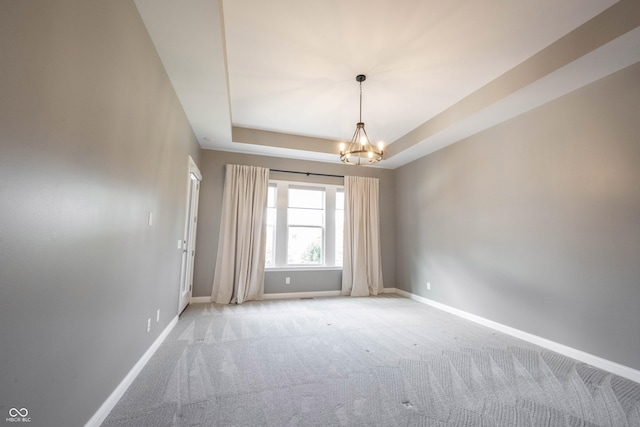 empty room with a raised ceiling, light carpet, a notable chandelier, and baseboards