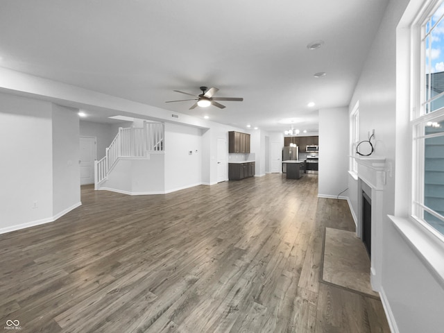 unfurnished living room featuring dark wood finished floors, stairway, a fireplace with flush hearth, a ceiling fan, and baseboards