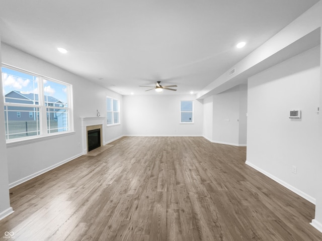 unfurnished living room featuring a fireplace with flush hearth, baseboards, ceiling fan, and wood finished floors