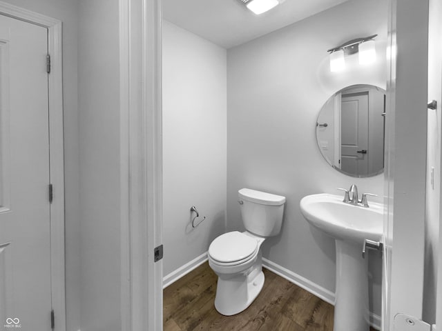 half bathroom featuring toilet, a sink, baseboards, and wood finished floors