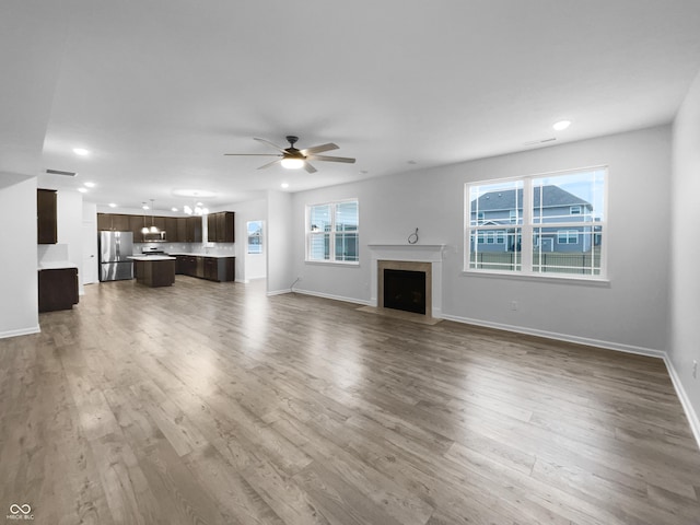 unfurnished living room featuring a fireplace with flush hearth, ceiling fan, wood finished floors, and visible vents