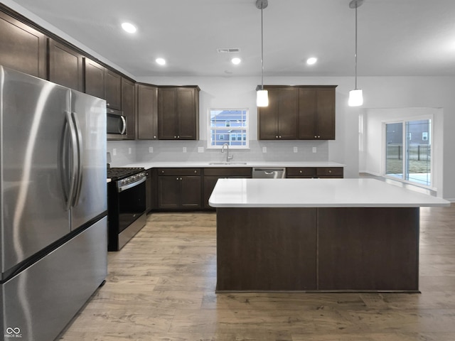 kitchen with dark brown cabinets, appliances with stainless steel finishes, light wood-style flooring, and decorative backsplash