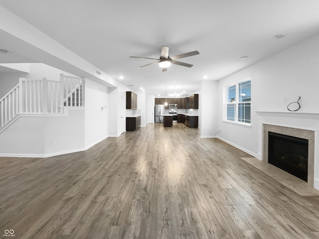 unfurnished living room with a fireplace, wood finished floors, a ceiling fan, baseboards, and stairs