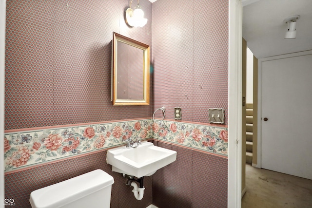 bathroom featuring a wainscoted wall, a sink, toilet, and wallpapered walls