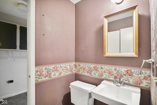 half bath featuring a sink, toilet, and wallpapered walls