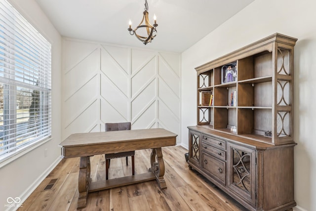 office with a decorative wall, visible vents, baseboards, light wood finished floors, and an inviting chandelier