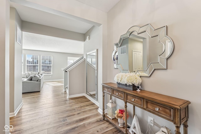 hallway with light wood finished floors, visible vents, and baseboards