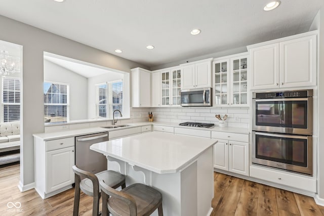 kitchen with a breakfast bar area, stainless steel appliances, a sink, light wood-style floors, and glass insert cabinets