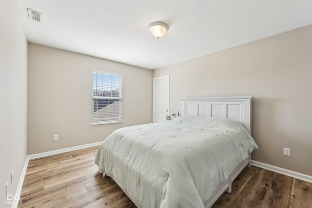 bedroom with a textured ceiling, wood finished floors, visible vents, and baseboards