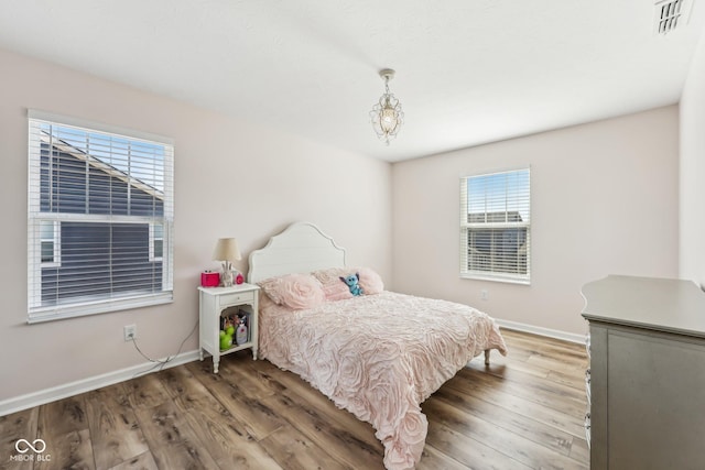 bedroom with wood finished floors, visible vents, and baseboards