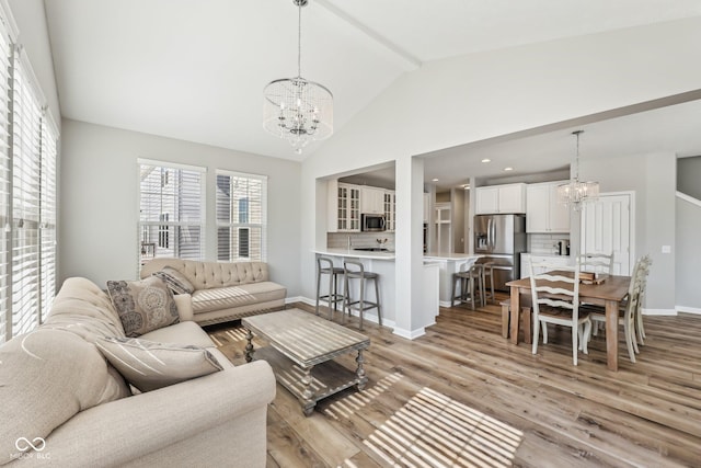 living area with baseboards, a chandelier, light wood-style flooring, beamed ceiling, and high vaulted ceiling