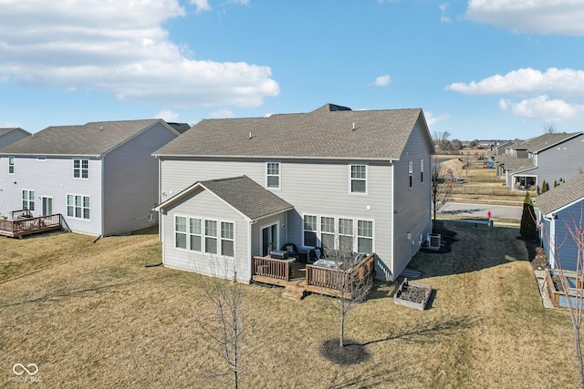 rear view of property featuring roof with shingles, central AC unit, a lawn, and a wooden deck