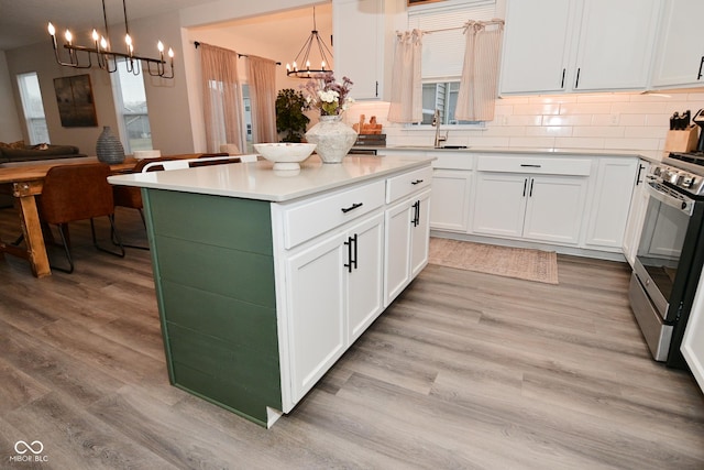 kitchen featuring a notable chandelier, light wood finished floors, white cabinets, stainless steel range oven, and a sink