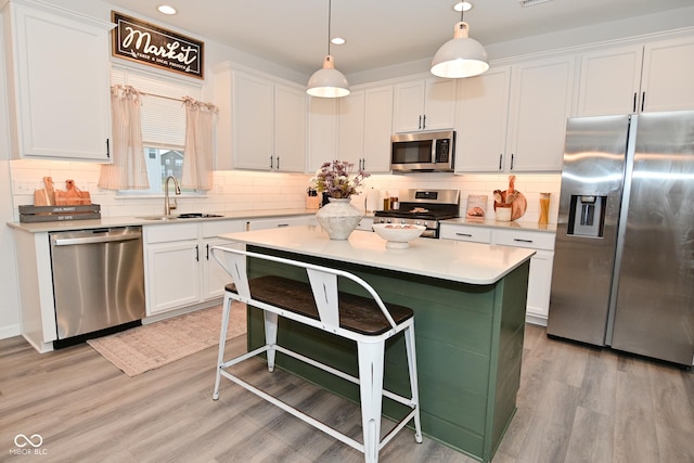 kitchen with light wood-style flooring, appliances with stainless steel finishes, a kitchen bar, white cabinetry, and a sink