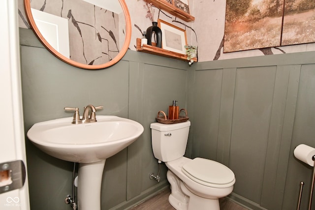 half bathroom featuring a decorative wall, toilet, and wood finished floors