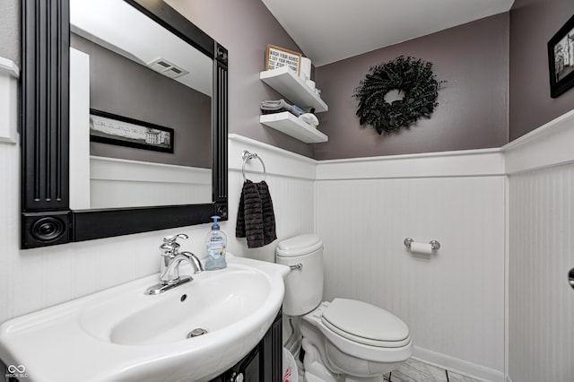 half bathroom featuring a wainscoted wall, visible vents, toilet, vaulted ceiling, and vanity