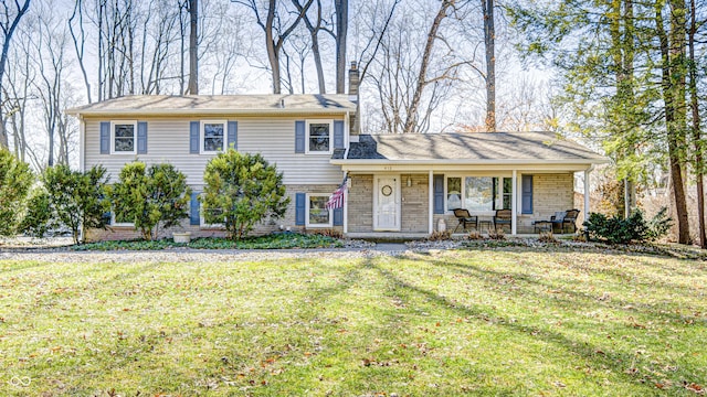 split level home featuring covered porch, brick siding, a chimney, and a front yard