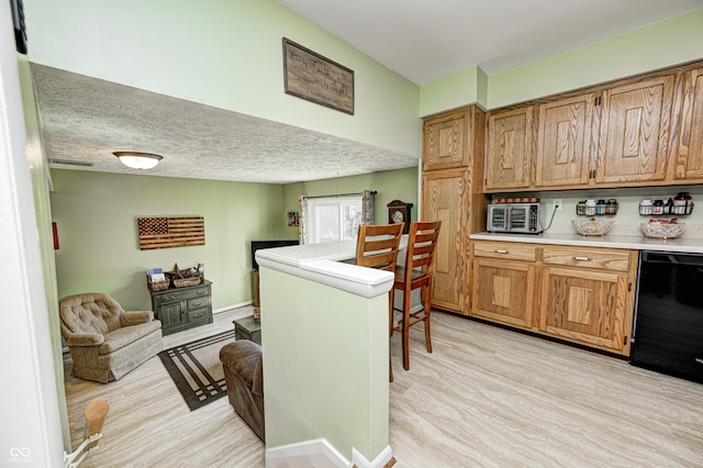 kitchen with a textured ceiling, light countertops, dishwasher, light wood finished floors, and brown cabinetry