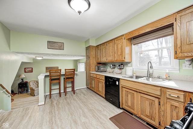 kitchen featuring light wood-type flooring, dishwasher, light countertops, and a sink