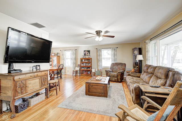 living room with light wood-style floors, baseboards, visible vents, and a ceiling fan