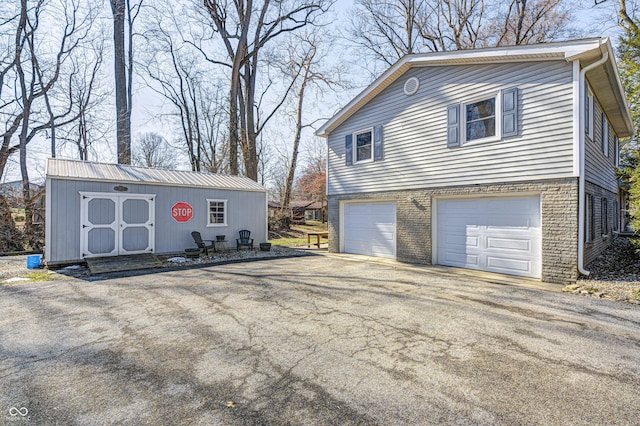 view of side of home with driveway, a garage, an outbuilding, and brick siding