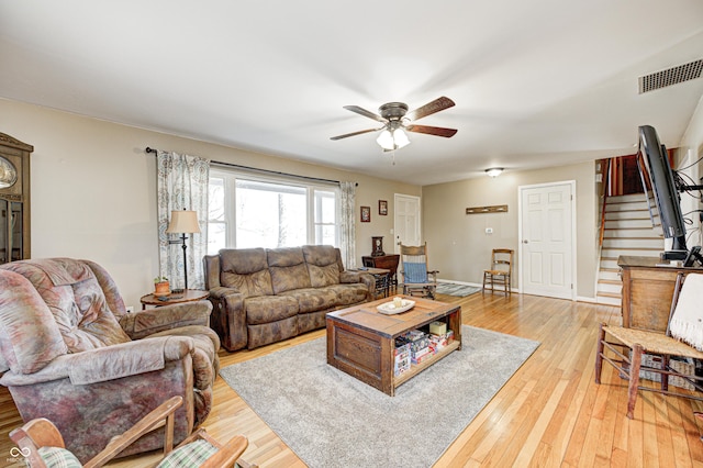 living area with visible vents, light wood-style flooring, stairway, a ceiling fan, and baseboards