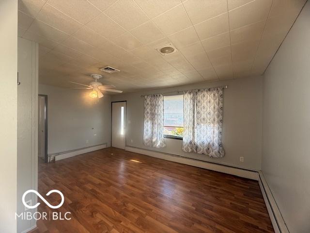 empty room featuring visible vents, baseboard heating, wood finished floors, and a ceiling fan