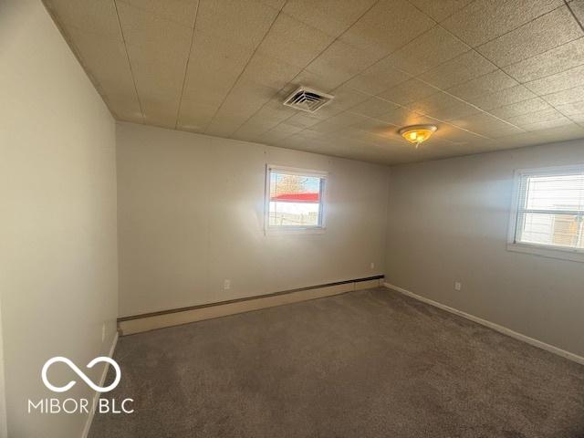 empty room with a wealth of natural light, a baseboard heating unit, carpet floors, and visible vents