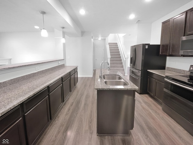 kitchen featuring a sink, light wood-style floors, dark brown cabinets, appliances with stainless steel finishes, and an island with sink