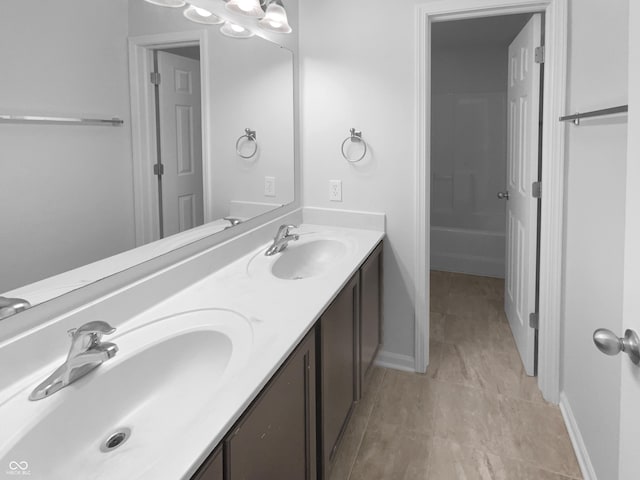 full bathroom with a bathtub, a sink, baseboards, and double vanity