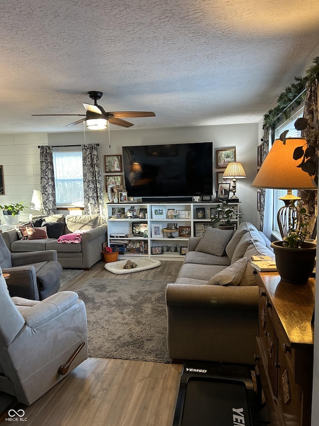 living area with a textured ceiling, a ceiling fan, and wood finished floors