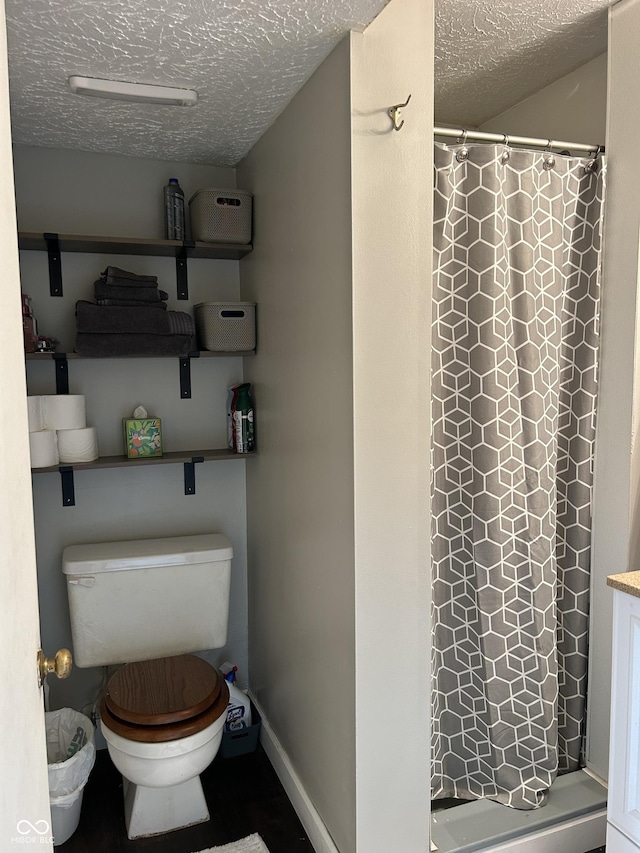 bathroom with a textured ceiling, a stall shower, toilet, and baseboards