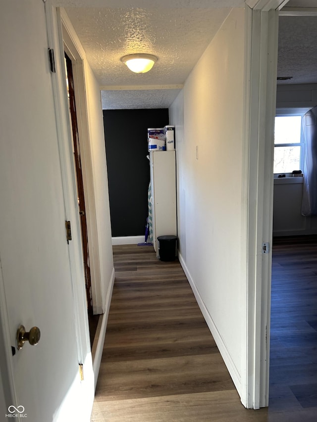 corridor featuring a textured ceiling, baseboards, and wood finished floors
