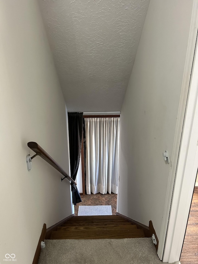 stairway with a textured ceiling and carpet flooring