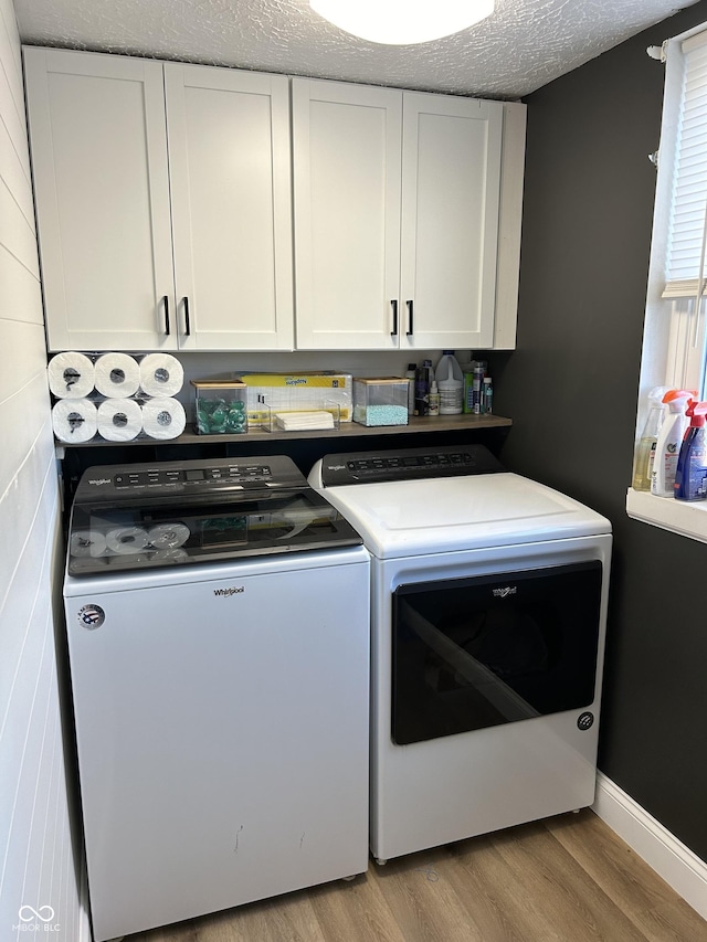 laundry room with washer and clothes dryer, cabinet space, a textured ceiling, light wood-type flooring, and baseboards