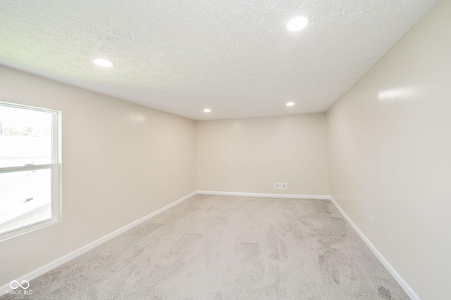 empty room featuring a textured ceiling, baseboards, a wealth of natural light, and light colored carpet