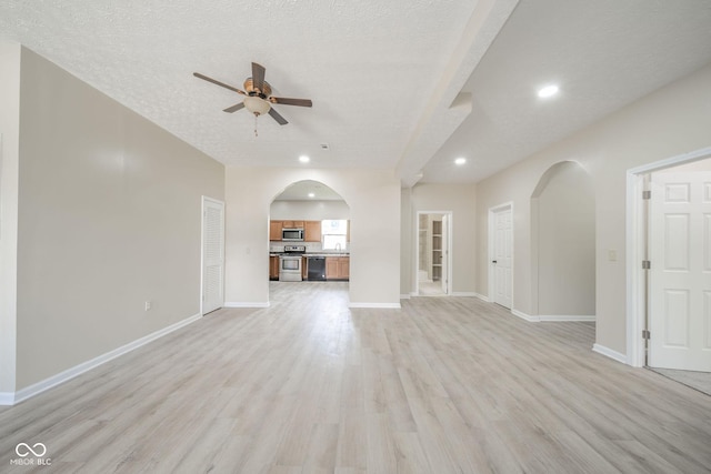 unfurnished living room with arched walkways, ceiling fan, a textured ceiling, light wood-style flooring, and baseboards