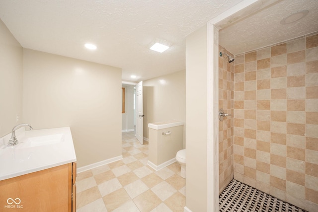 full bath featuring toilet, a tile shower, vanity, a textured ceiling, and baseboards