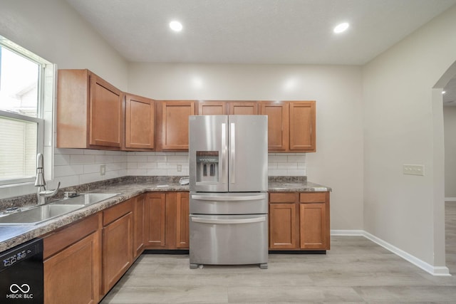 kitchen with brown cabinets, stainless steel refrigerator with ice dispenser, tasteful backsplash, a sink, and dishwasher